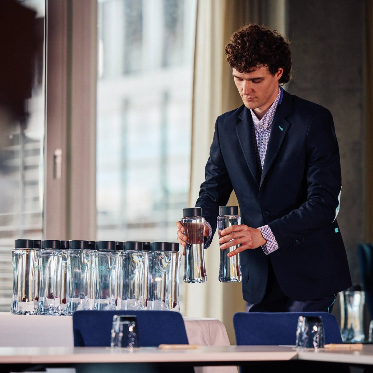 Un serveur en costume tenant Bouteilles d'eau, en train de préparer une table de réunion.
