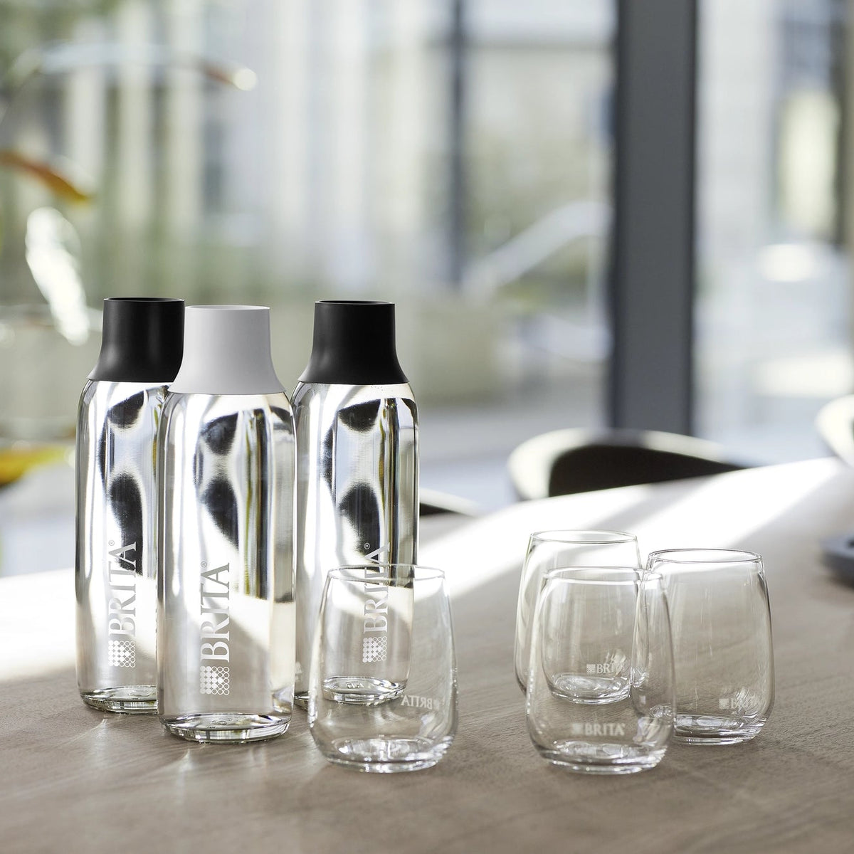 Des bouteilles et des verres BRITA Wave posés sur une table, avec un arrière-plan de bureau flou.