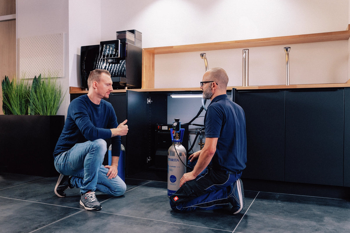 Two men working in a modern kitchen kneeling in front a BRITA CO₂ cylinder.