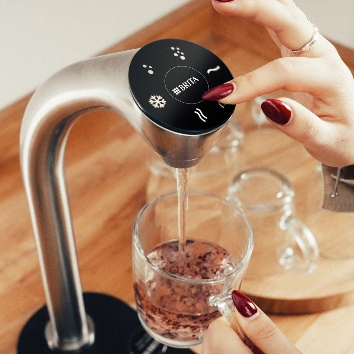 Une personne utilise un BRITA Extra C-Tap pour verser de l'eau chaude dans un verre contenant des feuilles de thé.