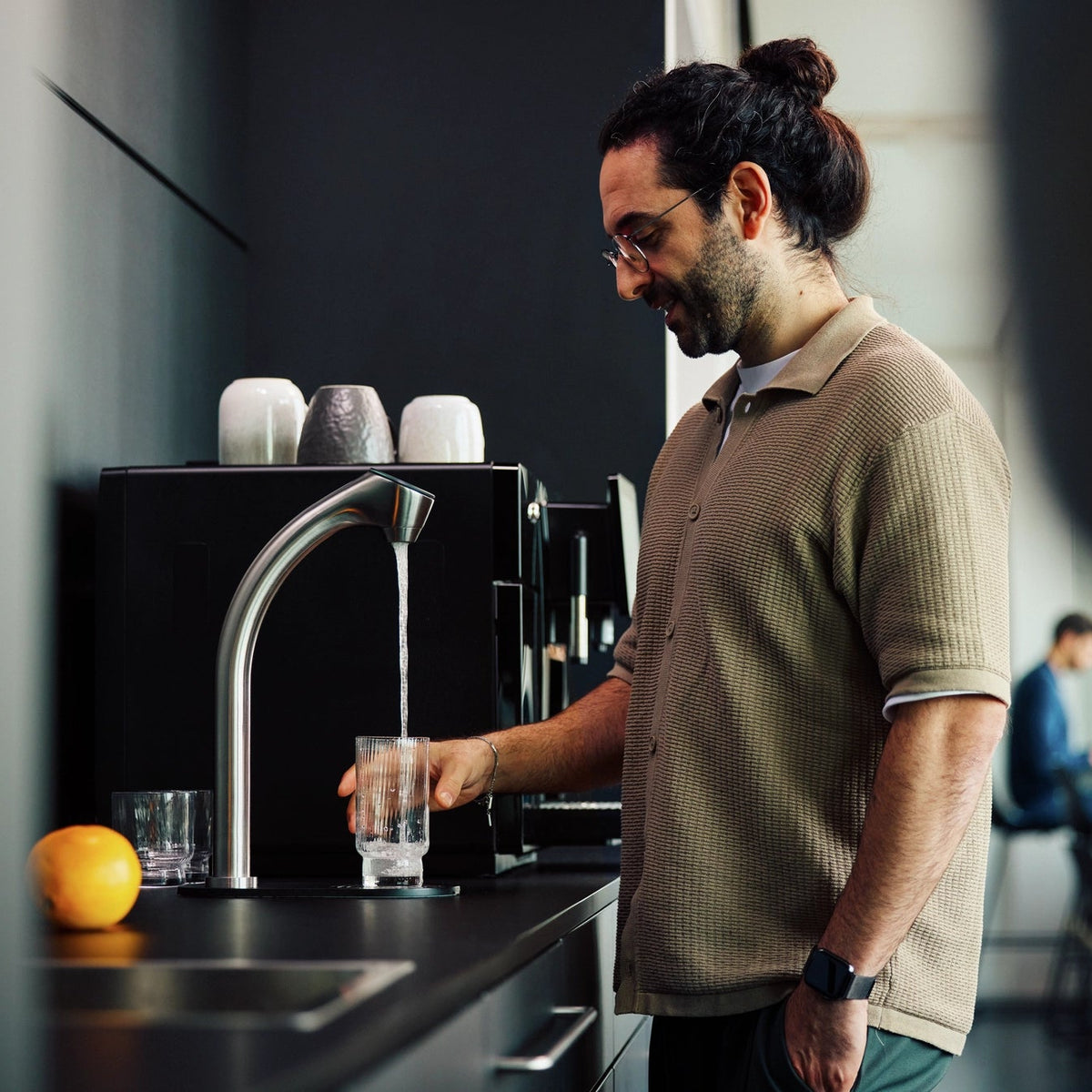 Un homme dans la cuisine d'un bureau en train de verser de l'eau d'un BRITA C-Tap dans un verre.
