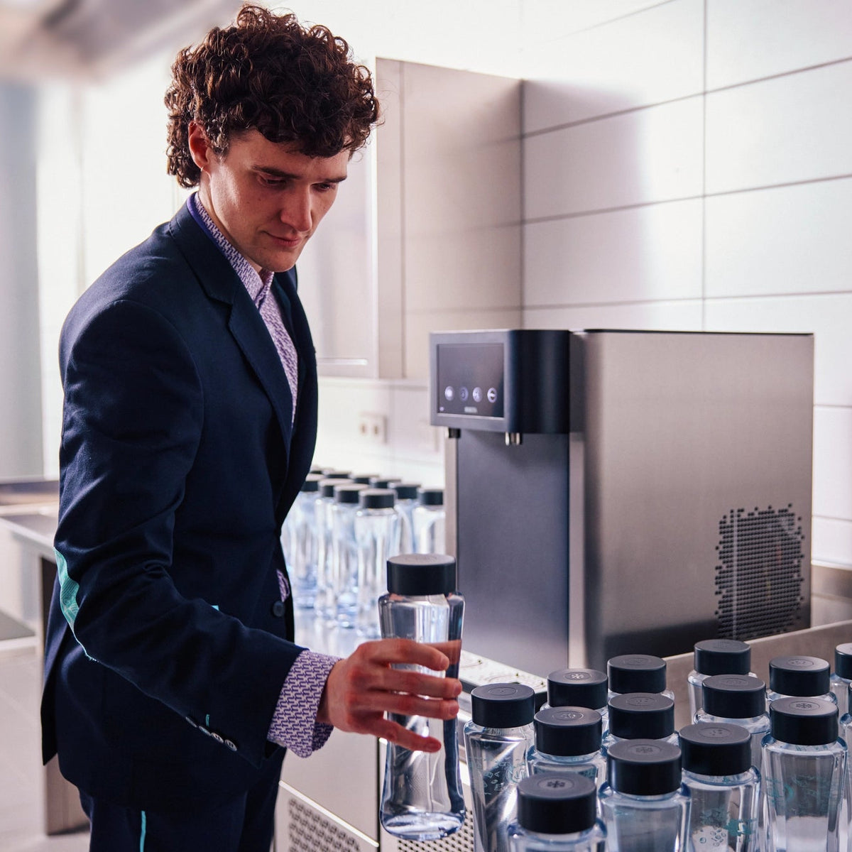 Un homme en costume se tient devant une fontaines à eau  BRITA Fill Pro, à côté de plusieurs bouteilles Twist.