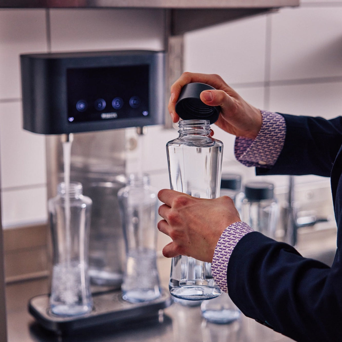 Une personne tenant une Bouteille Twist  BRITA Bouteille Twist  munie d'un bouchon foncé devant un BRITA Fill T-Tap.