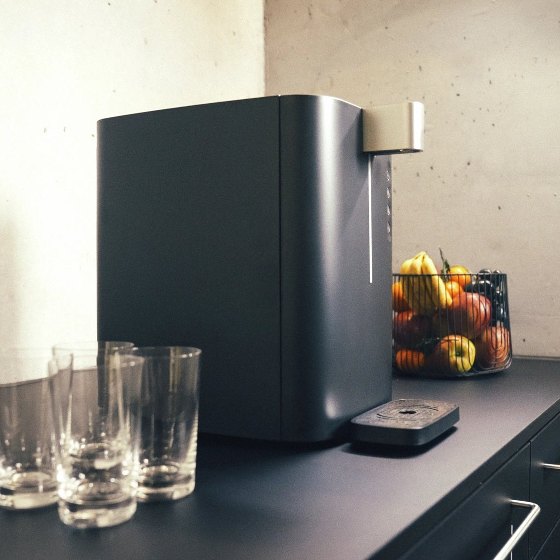 Un BRITA Top Compact posé sur un plan de travail de cuisine, avec des verres et une corbeille de fruits en arrière-plan.